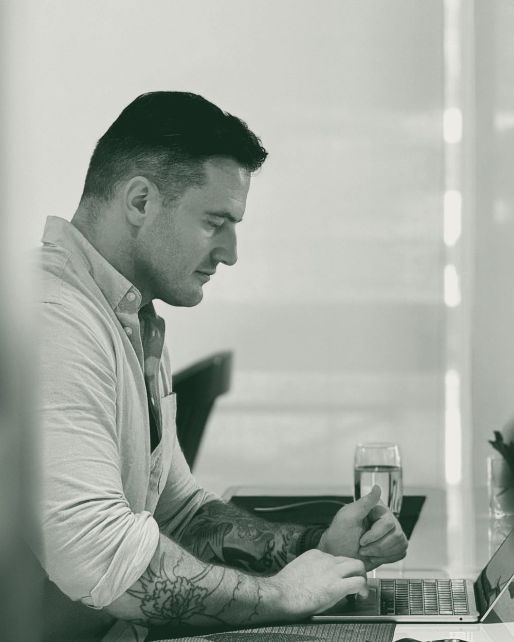 James Richman in profile at a table, working on a laptop beside a glass of water.